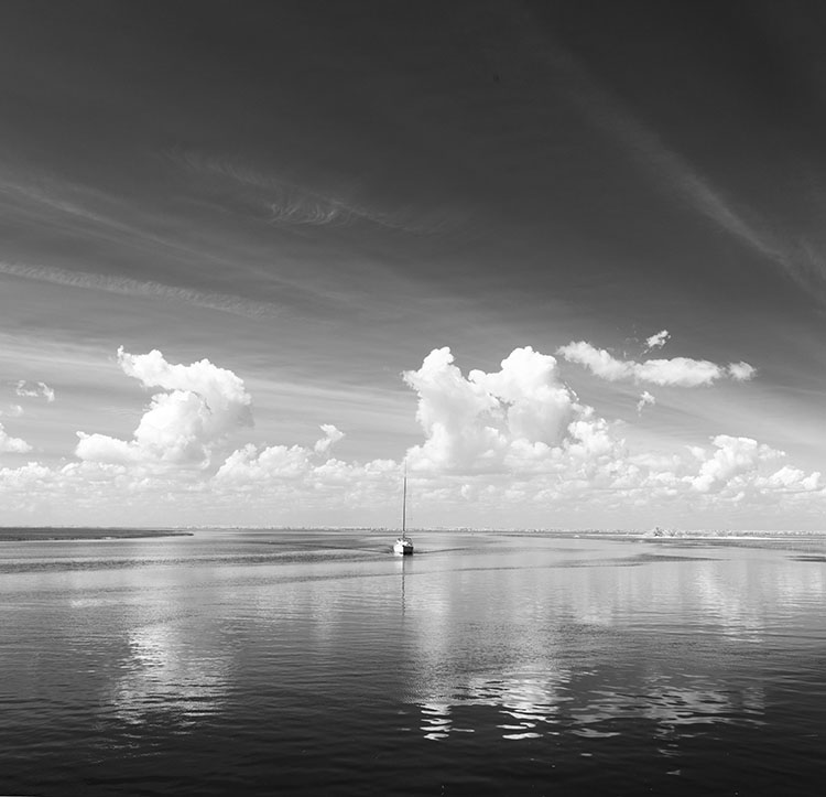 Infrared Head On Photo of Sailboat in Channel with Clouds.